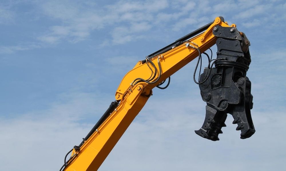 Yellow excavator arm with hydraulic crusher against sky