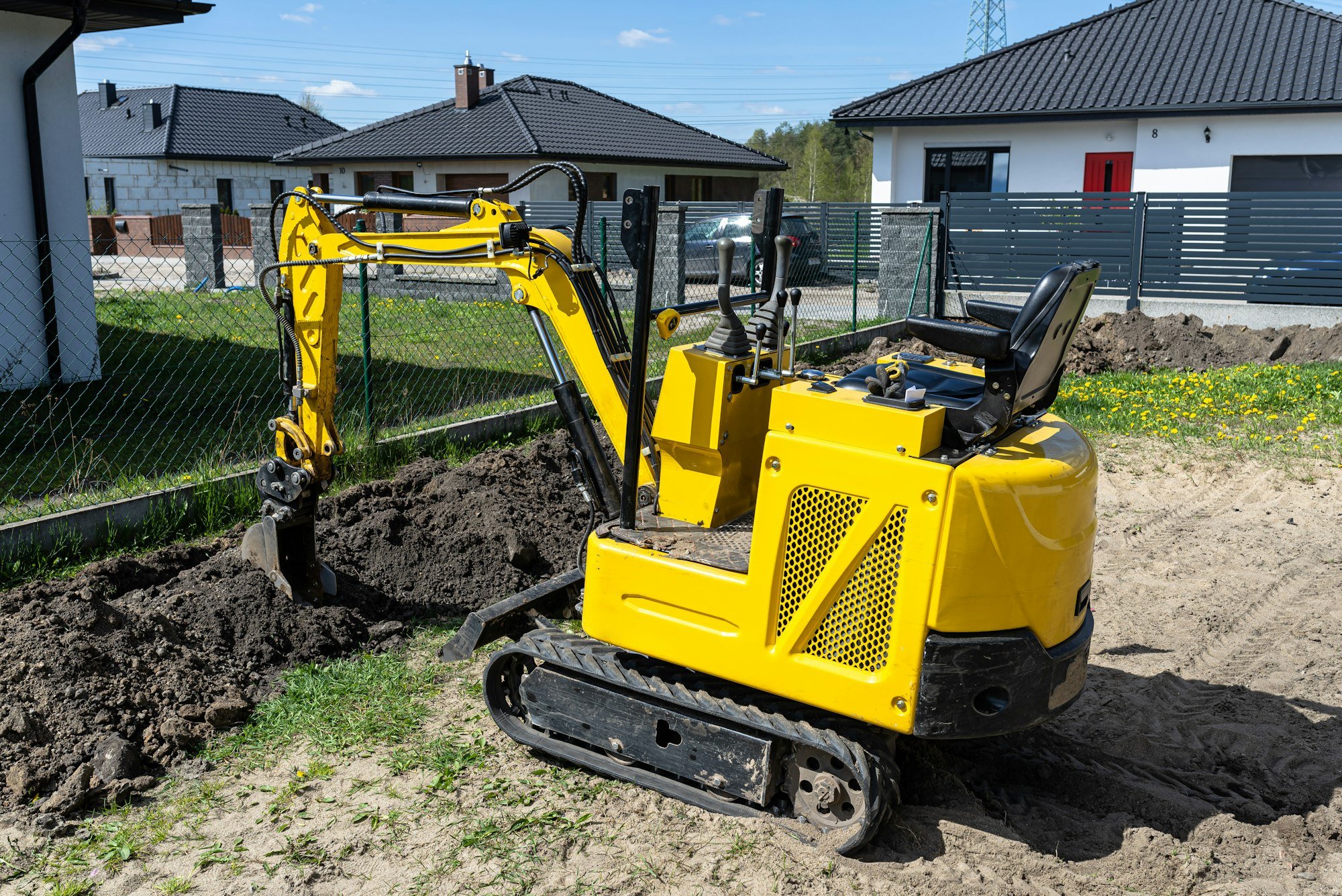 Mini digger digging a hole in the garden along the fence to the drainage pipes.