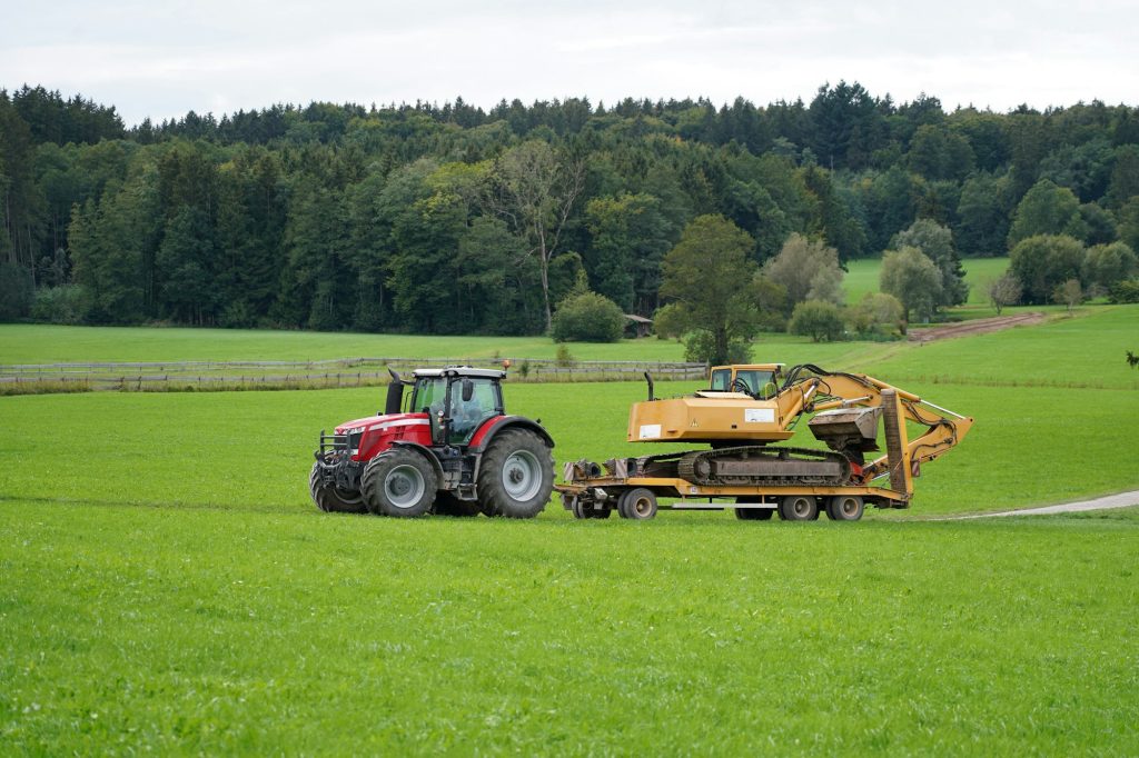 Old tractor towing an excavator on a field in Bavaria surrounded by green fields